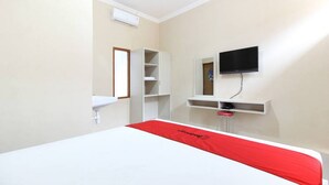 A hotel room with a bed, a TV mounted on the wall, a white wardrobe, and a small desk with a mirror. - RedDoorz near Balekambang City Park (Surakarta)