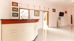 A reception area with a wooden counter, framed artwork on the walls, and a television on a cabinet. - RedDoorz near Balekambang City Park (Surakarta)