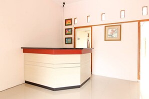 A reception area with a counter, framed artwork on the wall, and a door leading to another room. - RedDoorz near Balekambang City Park (Surakarta)