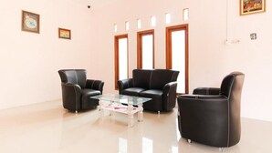 A modern living room with black leather sofas, a glass coffee table, and a large window with multiple panes. - RedDoorz near Balekambang City Park (Surakarta)