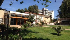 A modern building with large glass windows, a well-maintained garden, and a clear blue sky. - Mantagua Village (Quintero)