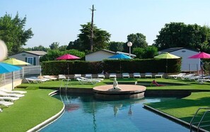 Una piscina con lettini e ombrelloni, circondata da vegetazione e un piccolo edificio.