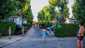 Une rue résidentielle bordée de maisons, avec des voitures garées et des enfants qui jouent.