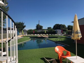 Una piscina con prato sintetico, lettini e ombrelloni.