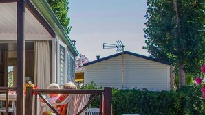 Une maison blanche avec des volets verts, une véranda dotée d’une balustrade et une cuisine visible.