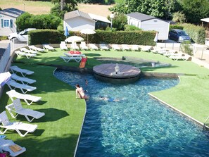 Una piscina con uno scivolo, circondata da poltrone a sdraio bianche e ombrelloni.