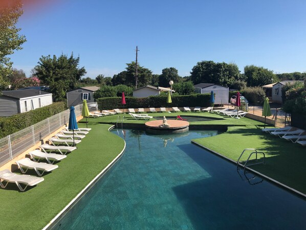 Area piscina con erba sintetica, poltrone da relax e ombrelloni.
