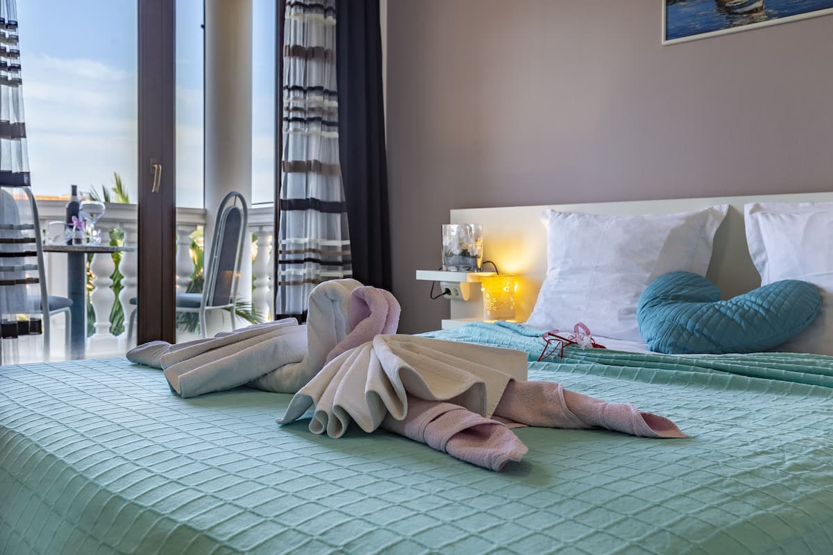 Une chambre d’hôtel avec un lit, une table de chevet avec une lampe, une fenêtre avec des rideaux et une vue sur l’extérieur.