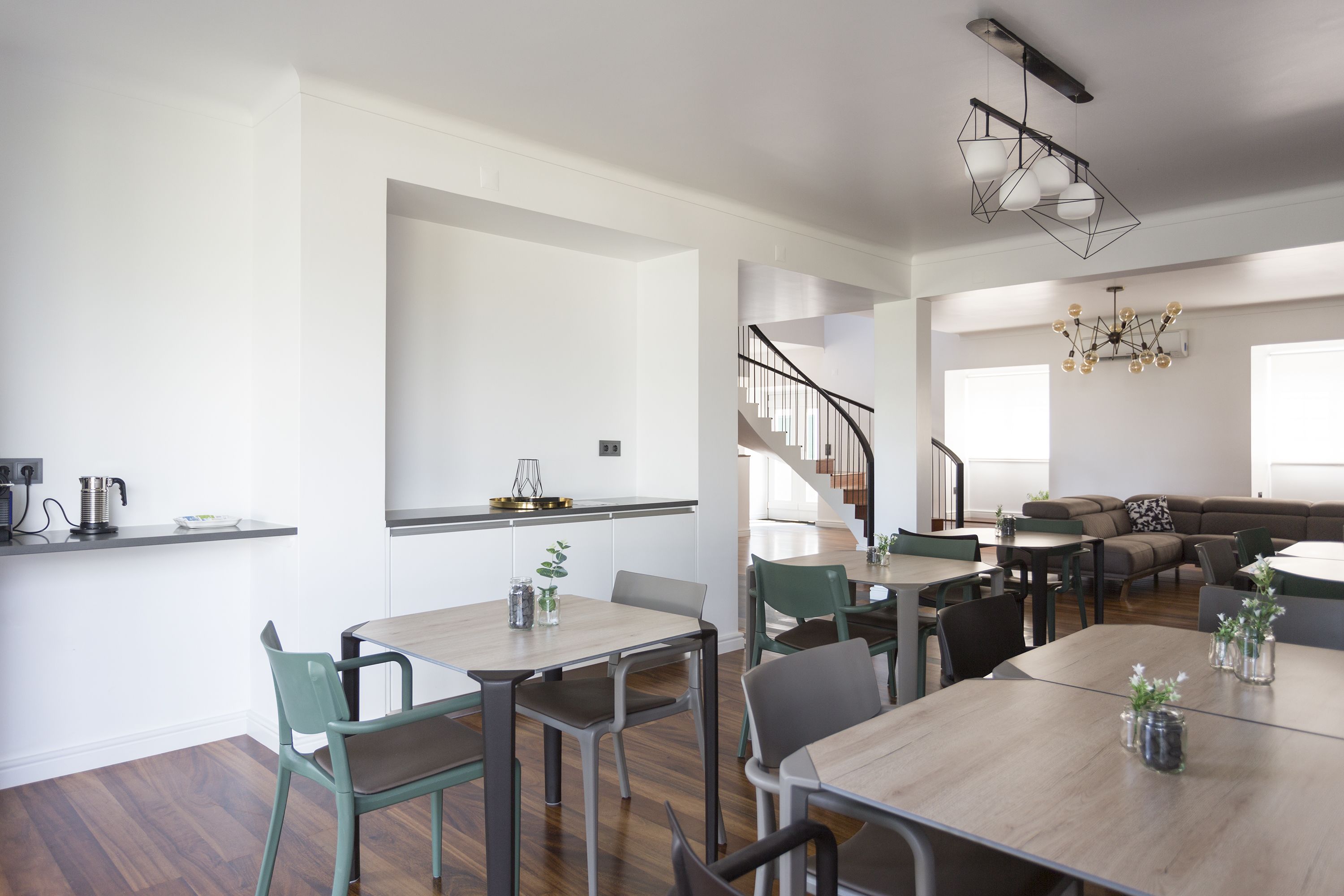 A modern kitchen with a built-in oven, a dining area with a wooden table and chairs, and a staircase leading to a living area with a sofa and a coffee table.