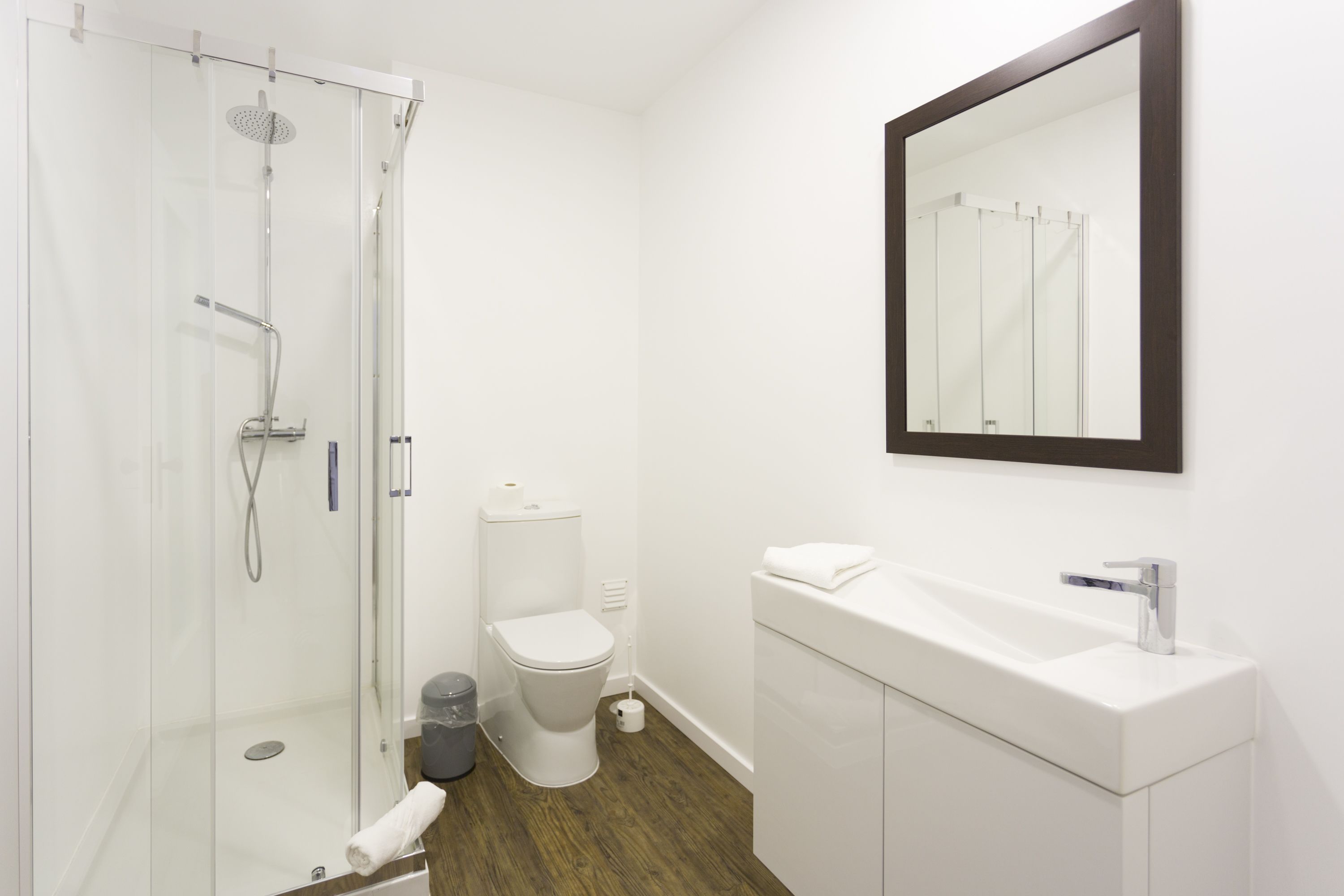 Un baño moderno con ducha envuelta en vidrio, inodoro blanco y lavamanos blanco con espejo arriba.