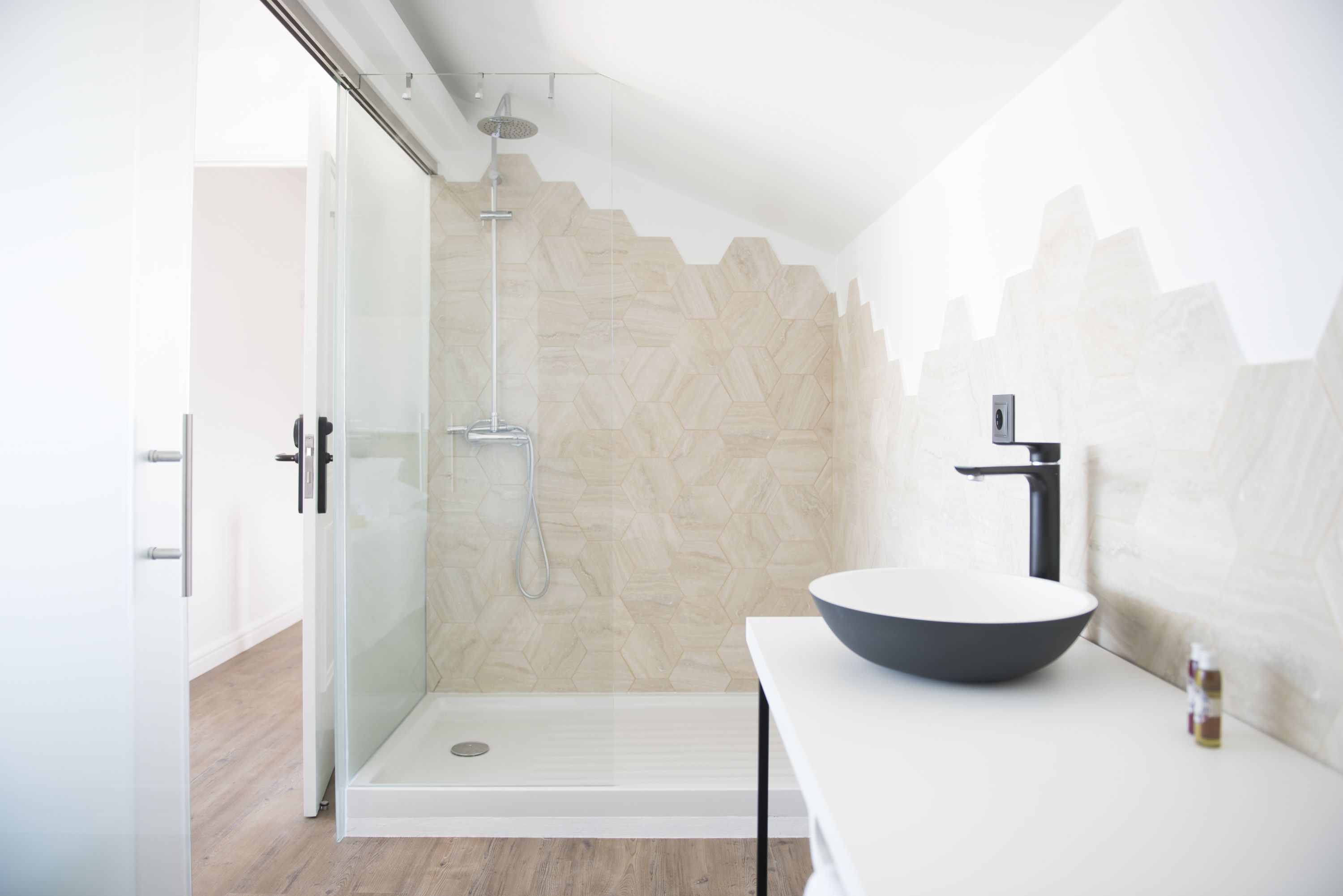 A modern bathroom with a glass shower enclosure, a white sink with a dark basin, and a herringbone-patterned wall.
