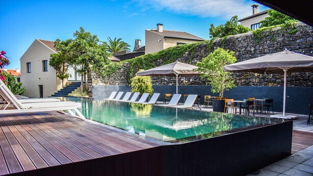 A modern outdoor pool area with lounge chairs, umbrellas, and a wooden deck. - Volcanic Charming House (Ribeira Grande)