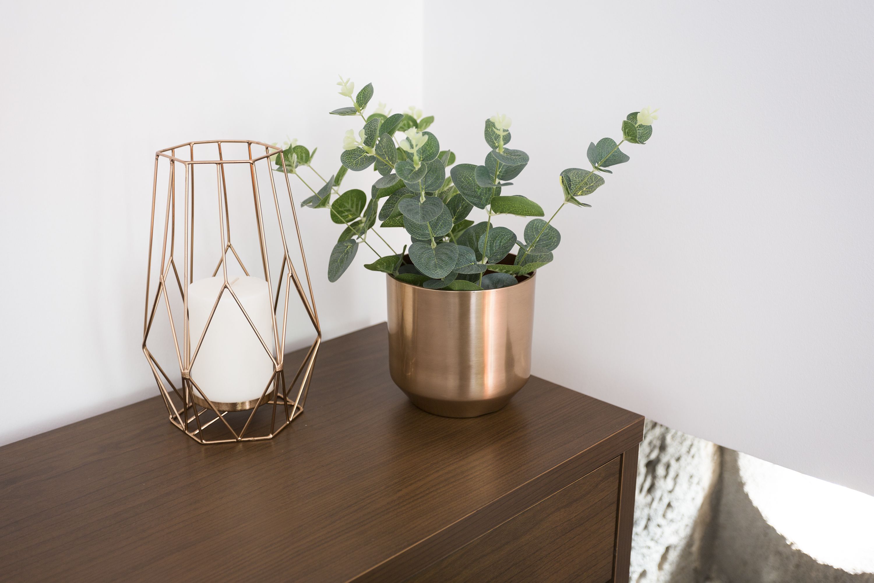 Een houten bijzettafeltje met een metalen vaas en een plant.
