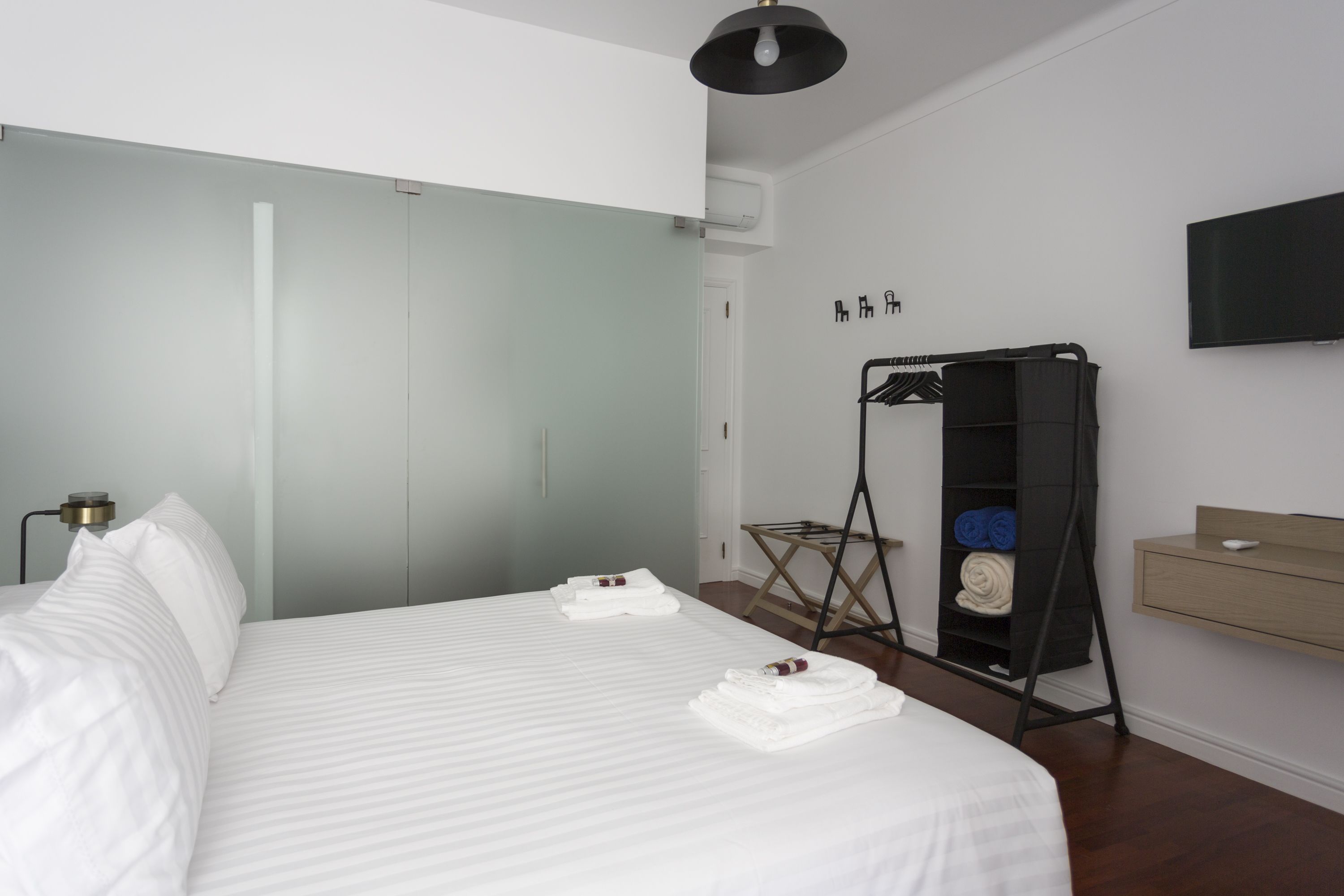 Une chambre d’hôtel moderne équipée d’un grand lit, d’une armoire, d’une télévision et d’une étagère avec des serviettes.