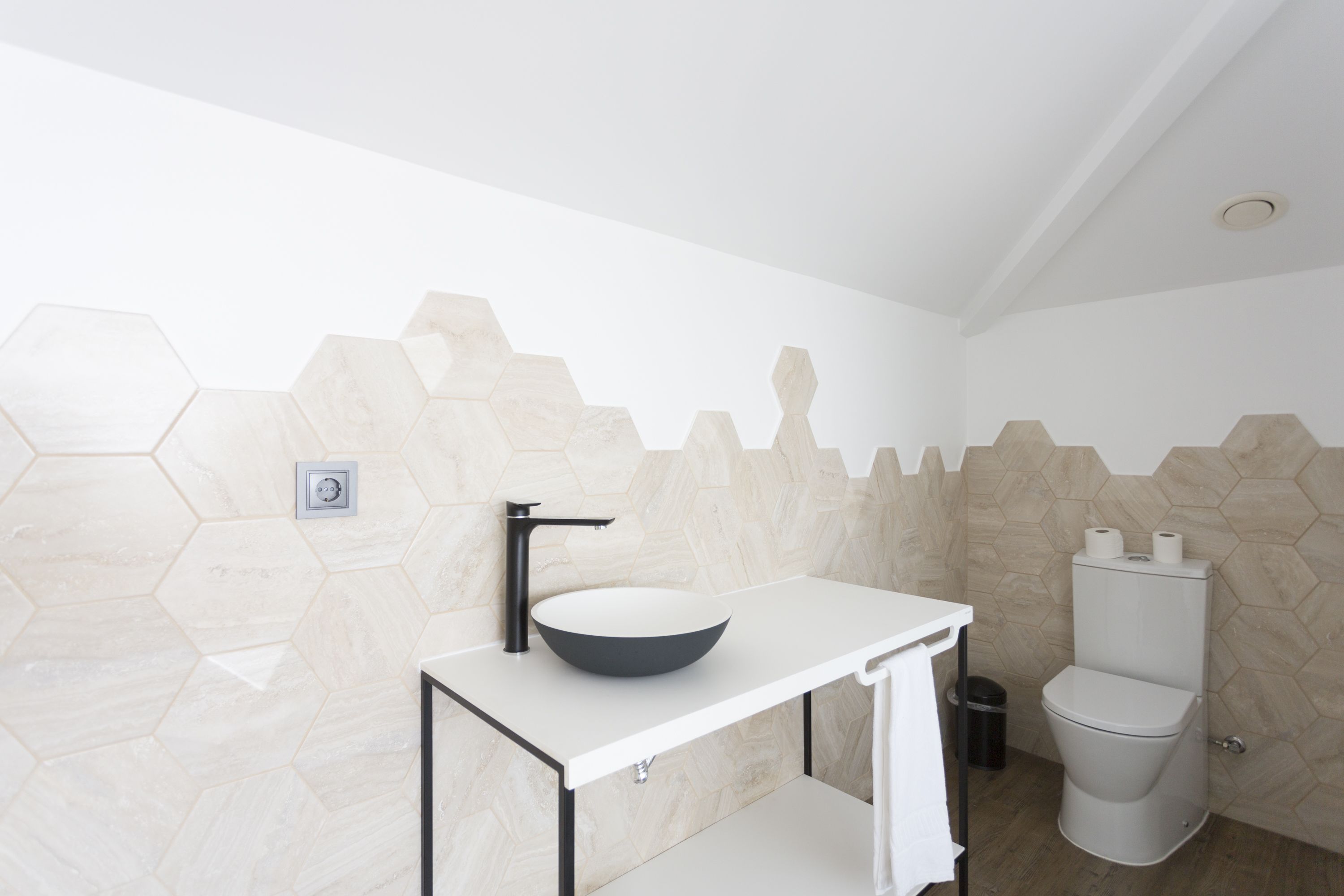 Un baño moderno con un lavamanos blanco, un grifo negro y un inodoro.