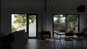 A modern interior with a sofa, dining table, chairs, and large windows offering views of the outdoors. - Volcanic Charming House (Ribeira Grande)
