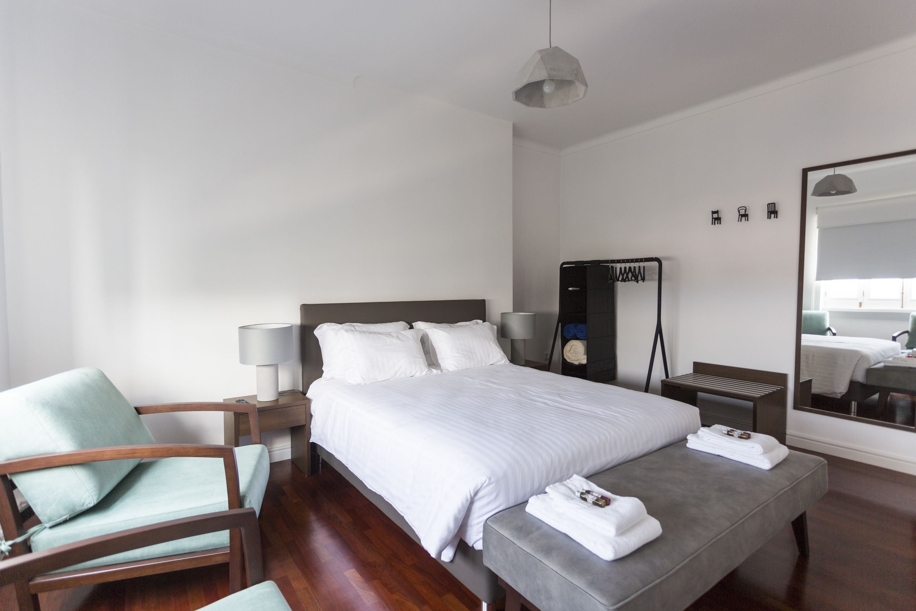 Ein modernes Hotelzimmer mit einem großen Bett, einer Sitzecke mit einem Sessel, einem Nachttisch mit Lampe, einem Spiegel und einem kleinen Tisch ebenfalls mit Lampe.