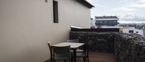 A rooftop terrace with a table and chairs, a stone wall, and a view of buildings in the distance.