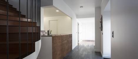 A modern interior with a wooden staircase, a kitchen area, and a hallway with patterned flooring.