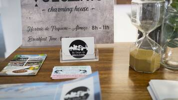 A wooden table with a sign for VOLCANIC charming house, brochures, and an hourglass.