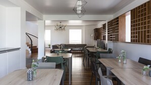 A modern kitchen with wooden countertops, a dining area with round tables and chairs, and a built-in bookshelf. - Volcanic Charming House (Ribeira Grande)