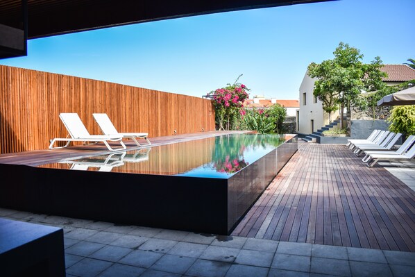 A modern outdoor pool area with wooden decking, lounge chairs, and a wooden wall. - Volcanic Charming House (Ribeira Grande)