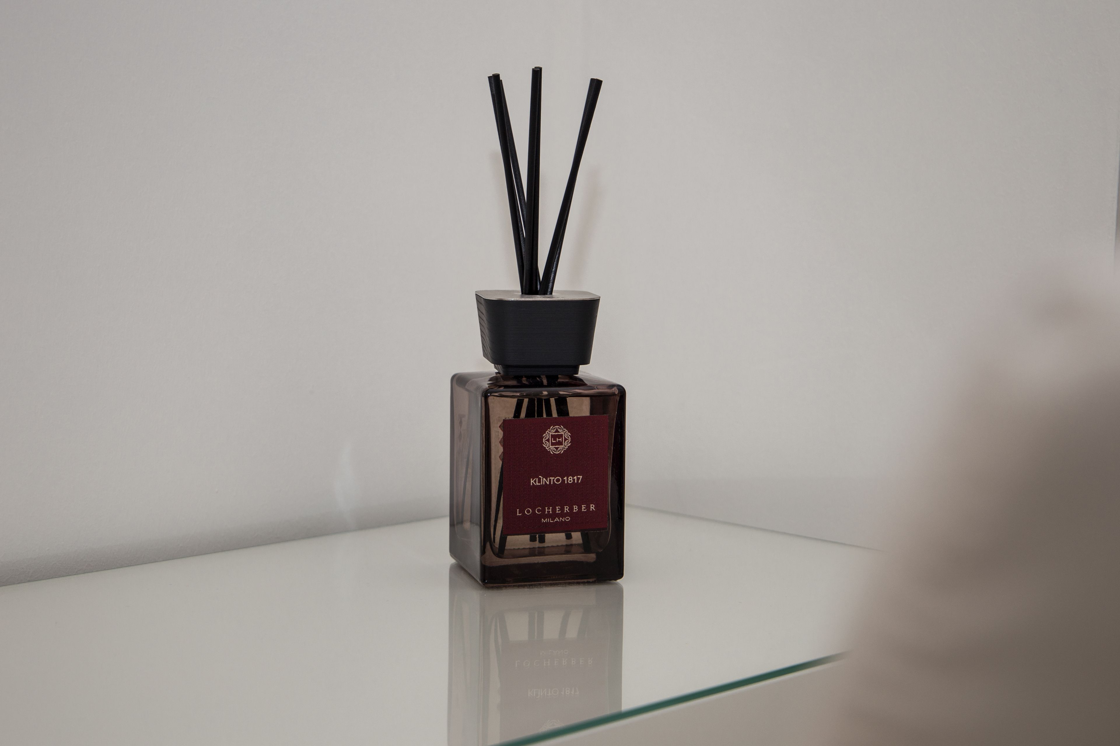 A bottle of Locherber Milano cologne with black reed diffusers on a reflective surface.