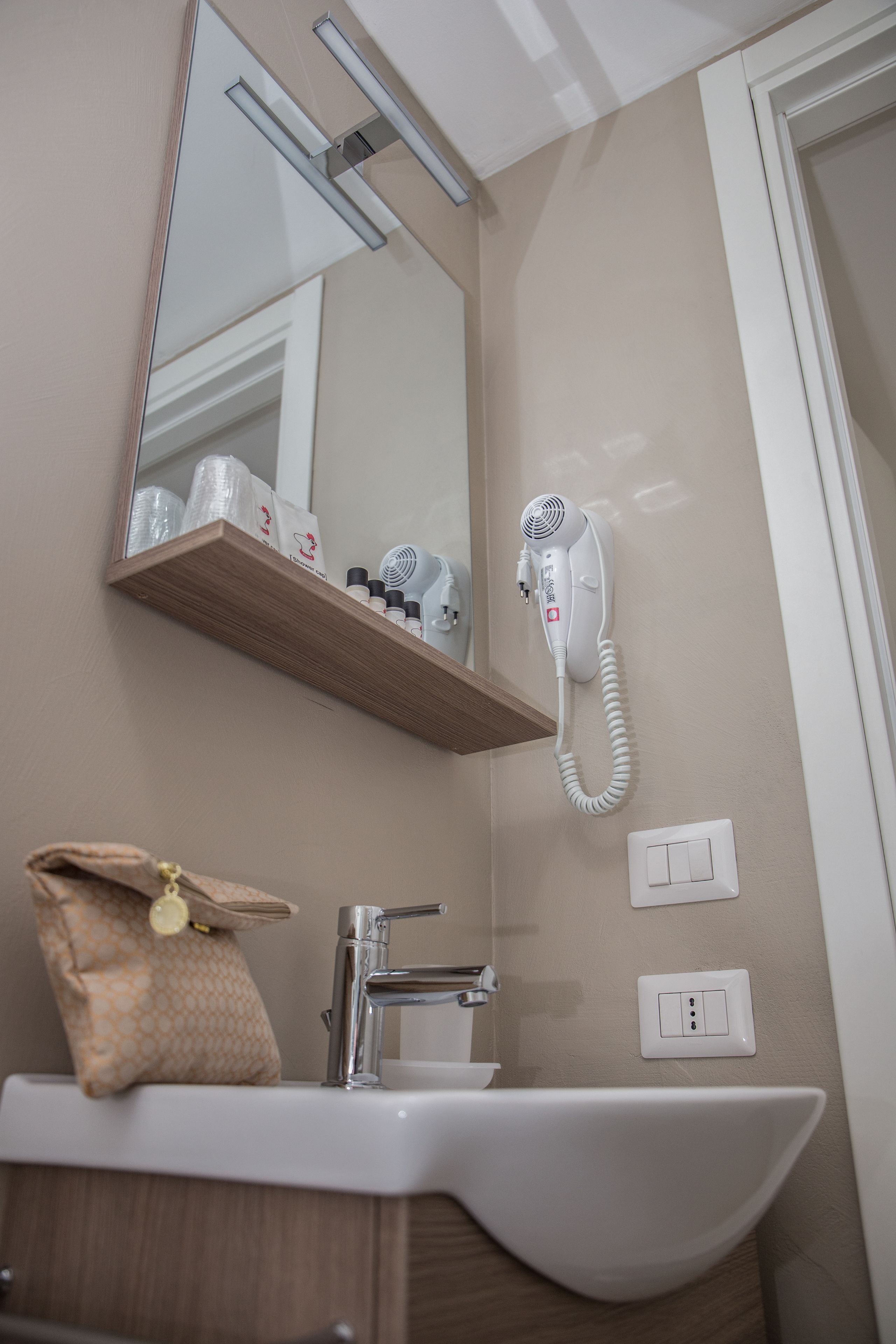 A bathroom with a sink, mirror, hairdryer, and a shelf with toiletries.