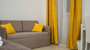 A neutral-colored sofa with two yellow pillows, a white side table, and yellow curtains. - La Civita B&B (Gravina in Puglia)