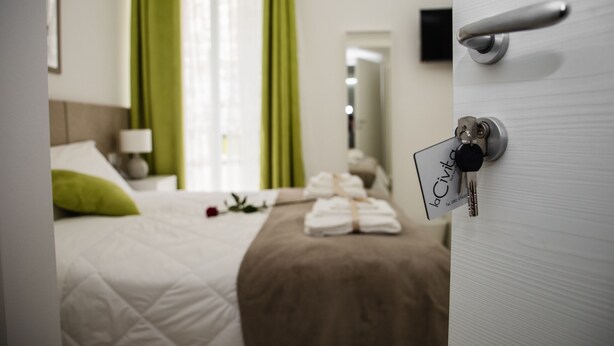 A hotel room with a neatly made bed, a green curtain, and a door with a key card lock. - La Civita B&B (Gravina in Puglia)