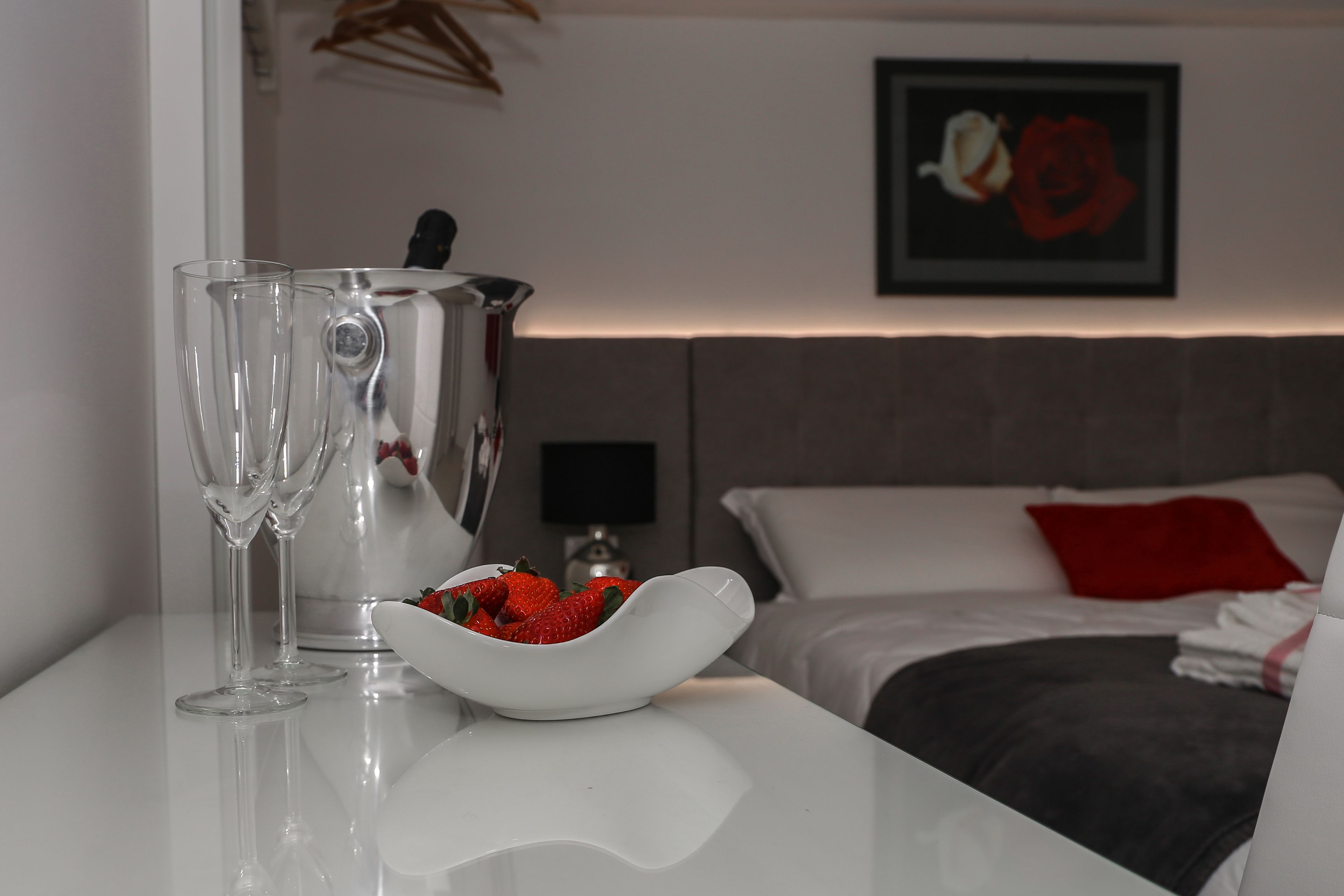 Ein modernes Hotelzimmer mit einem ordentlich bezogenem Bett, einem Nachttisch mit einer Schale Erdbeeren und zwei Gläsern.