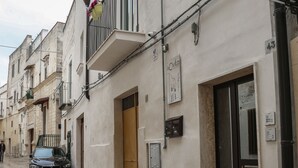 A narrow street with a parked car, buildings with balconies, and a sign indicating a business. - La Civita B&B (Gravina in Puglia)