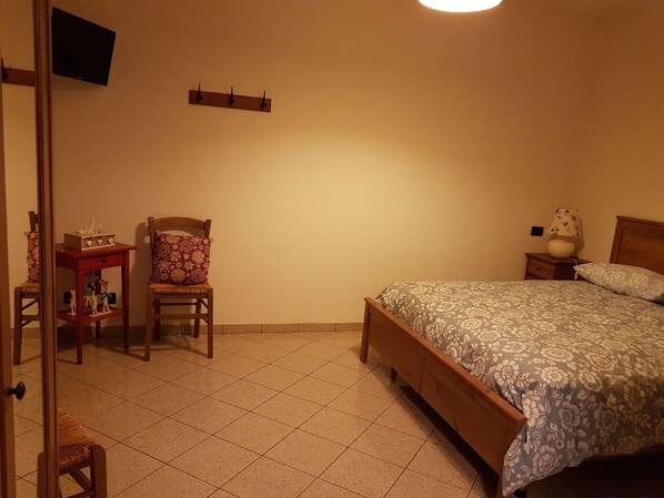 Un dormitorio con cama, una silla, una mesita de noche y un televisor montado en la pared.
