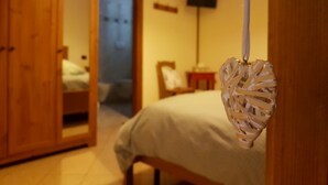 A bedroom with a bed, a wooden wardrobe, a heart-shaped decoration, and a television on the wall. - Azienda Agrituristica Lavagè (Rossiglione)