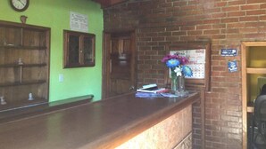 A reception area with a wooden counter, a clock, and a bulletin board. - Posada de Don Jose (Panajachel)