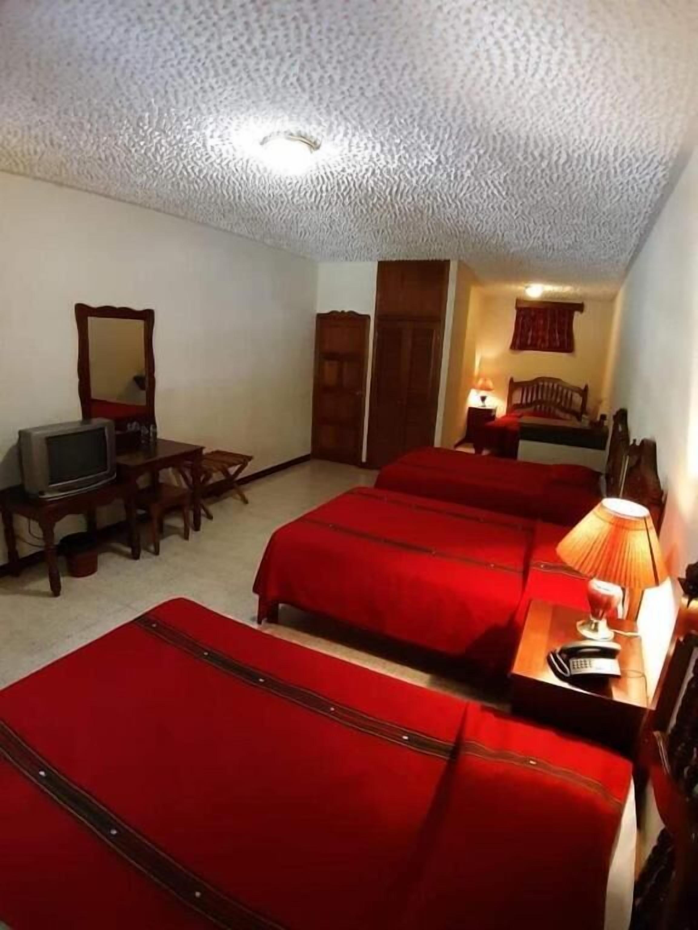 Habitación de hotel con tres camas, televisión, escritorio con lámpara y armario.