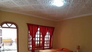 A hotel room with two beds, a wooden desk, a window with red curtains, and a decorative ceiling. - Posada de Don Jose (Panajachel)