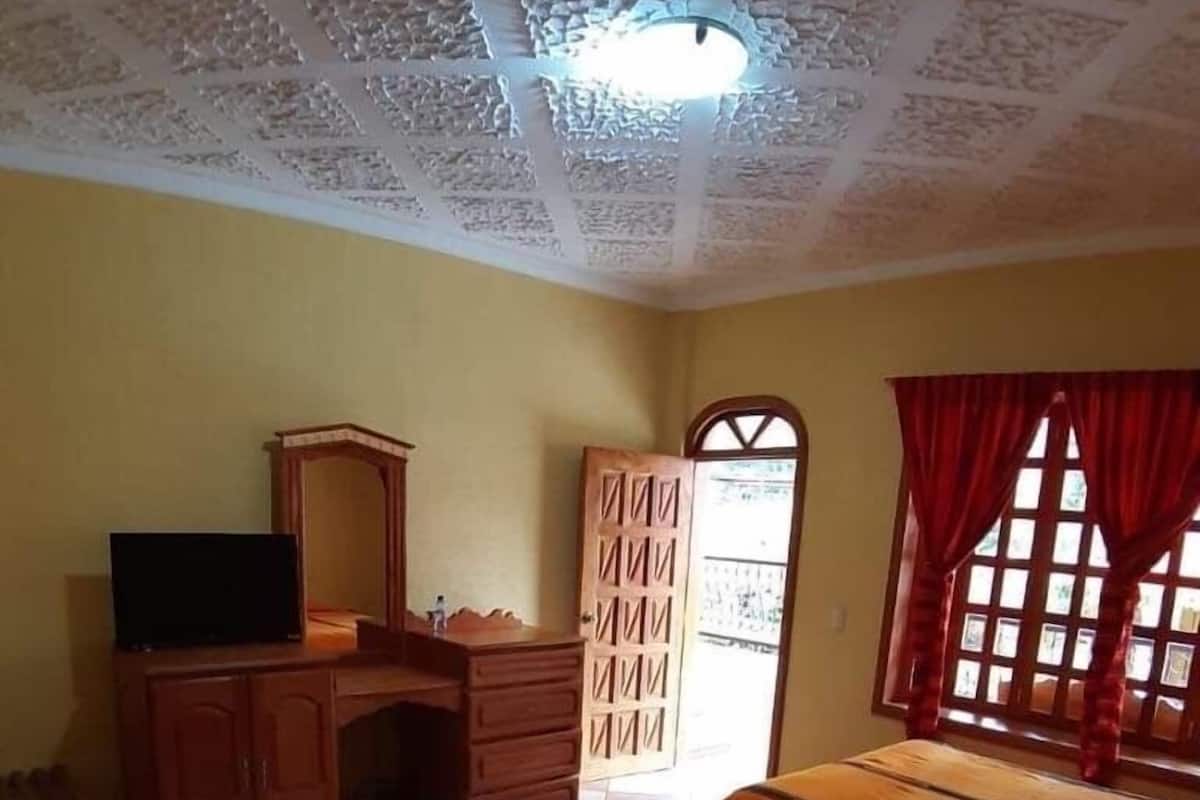 A room with two beds, a wooden dresser, a television, and a door with a window.