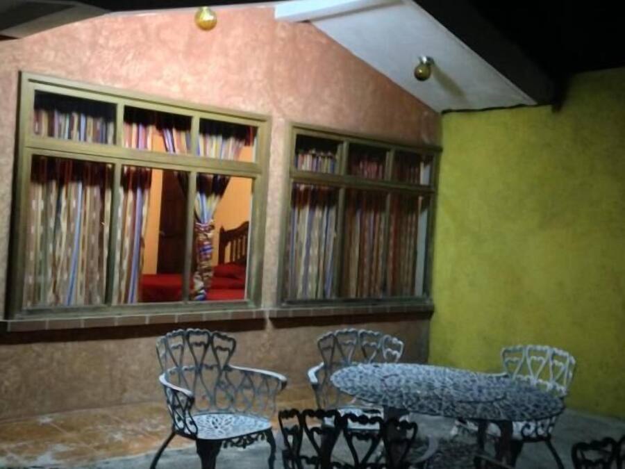A dining area with metal chairs and a round table, a window with curtains, and a yellow wall.