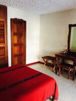 Una habitación con cama, escritorio de madera, silla y espejo.