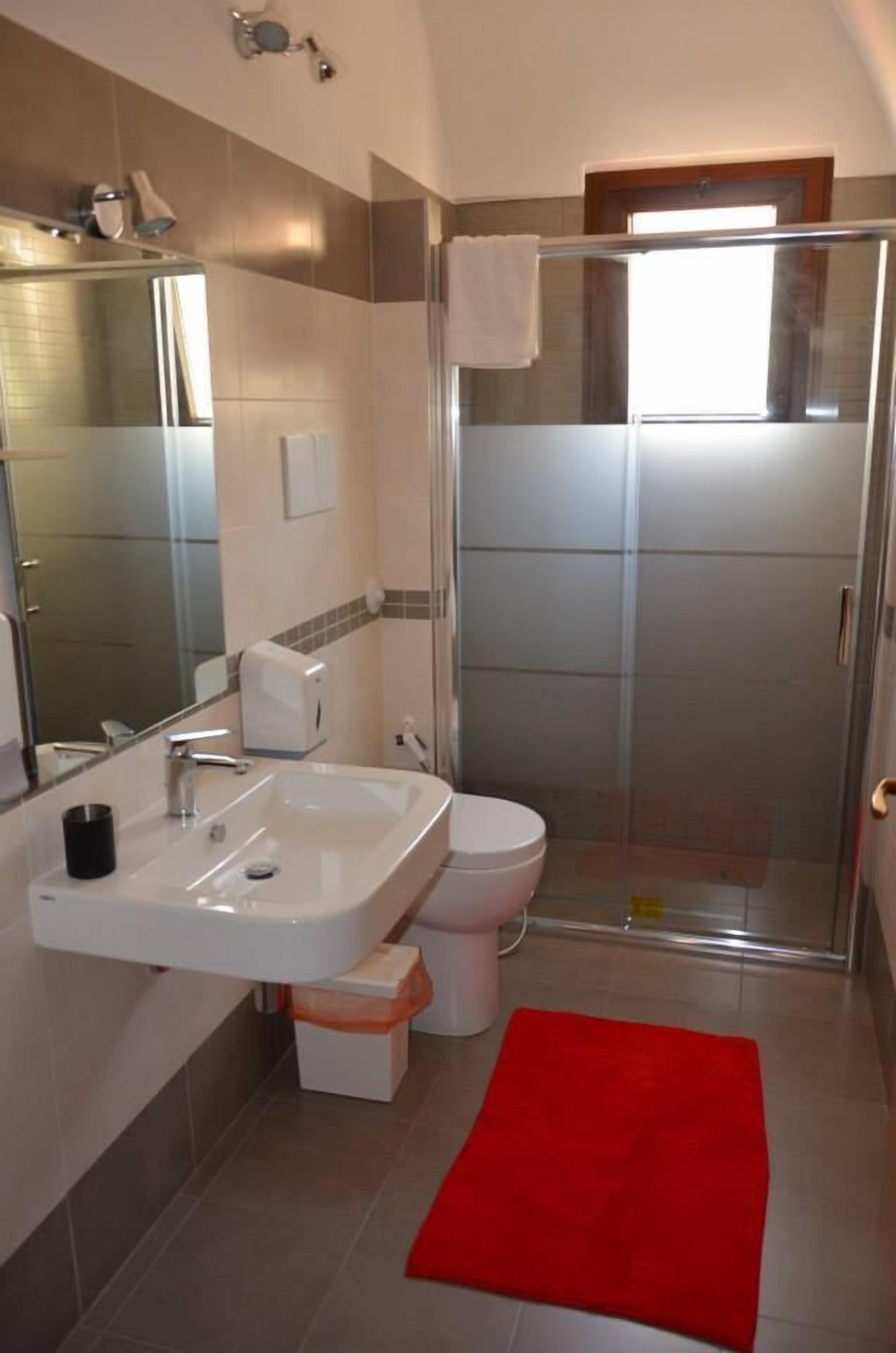 Ein modernes Badezimmer mit Duschkabine aus Glas, einem weißen Waschbecken und einer roten Badematte.