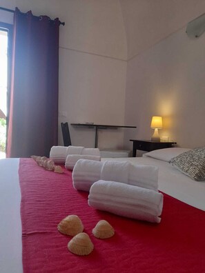 A hotel room with a bed, a nightstand, a lamp, and a view of the outdoors. - Ro.Ri Rooms (San Vito Lo Capo)