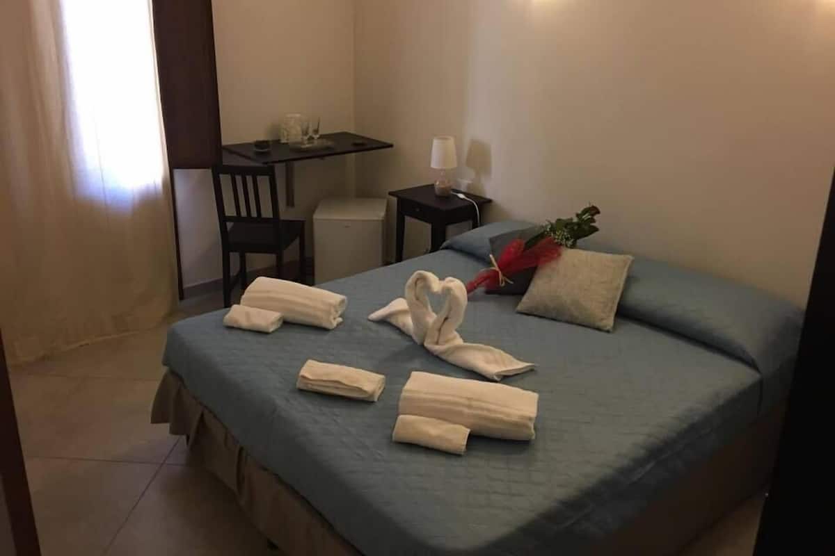 A hotel room with a bed, a desk, a chair, and a small table.