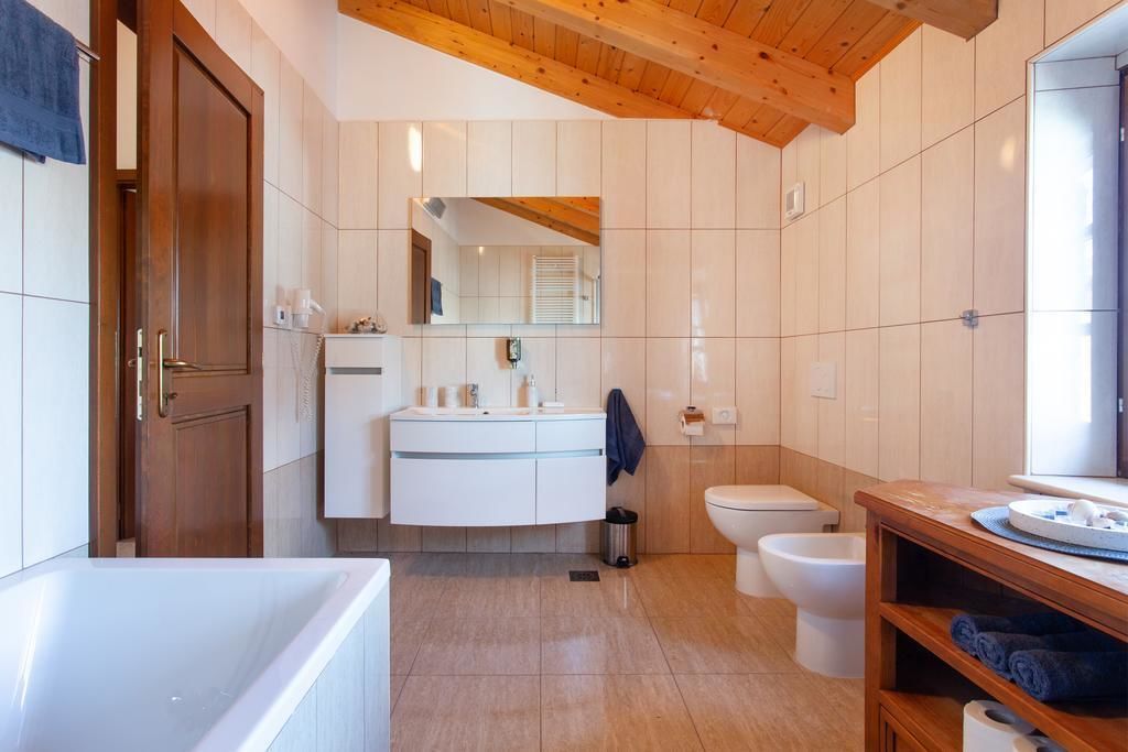 Un baño moderno con techo de madera, azulejos blancos, una bañera, un inodoro y un lavamanos con espejo.