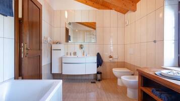 Un baño moderno con techo de madera, azulejos blancos, una bañera, un inodoro y un lavamanos con espejo.