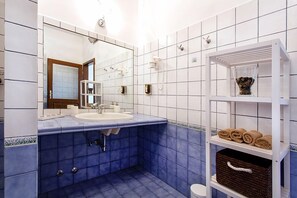 A bathroom with a white sink, blue tiles, a mirror, and a shelf with towels and a basket. - Residence Gold Istra (Piran)