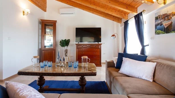 A living room with a wooden ceiling, a television, a cabinet, a sofa, and a coffee table with decorative items.