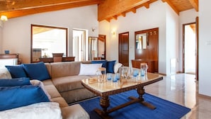 A spacious living room with a wooden ceiling, a large sofa, a coffee table, and a view of the outside.