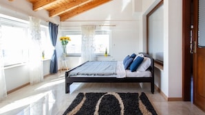 A bedroom with a bed, wooden ceiling beams, a window with curtains, and a view of the outside.