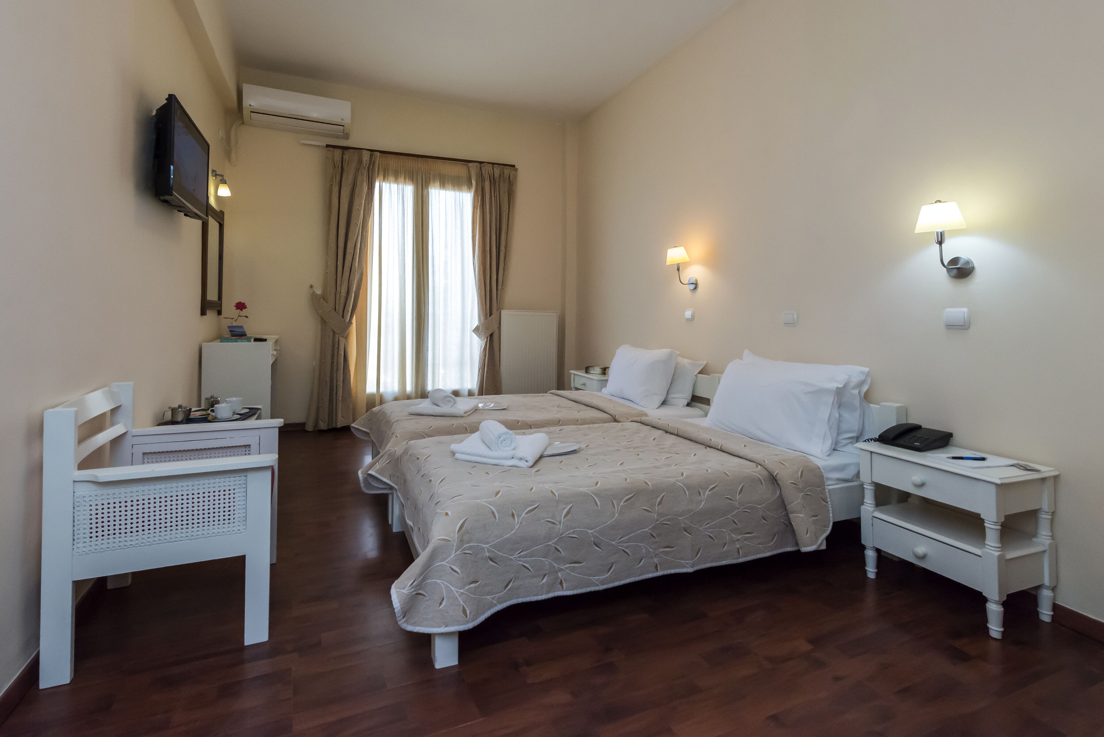 A hotel room with two beds, a desk, a chair, a TV, and a nightstand with a lamp.